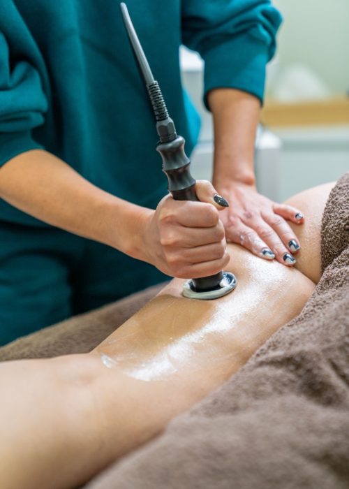 Beautician performing body radiofrequency on the patient's leg for cellulite reduction and skin firming.